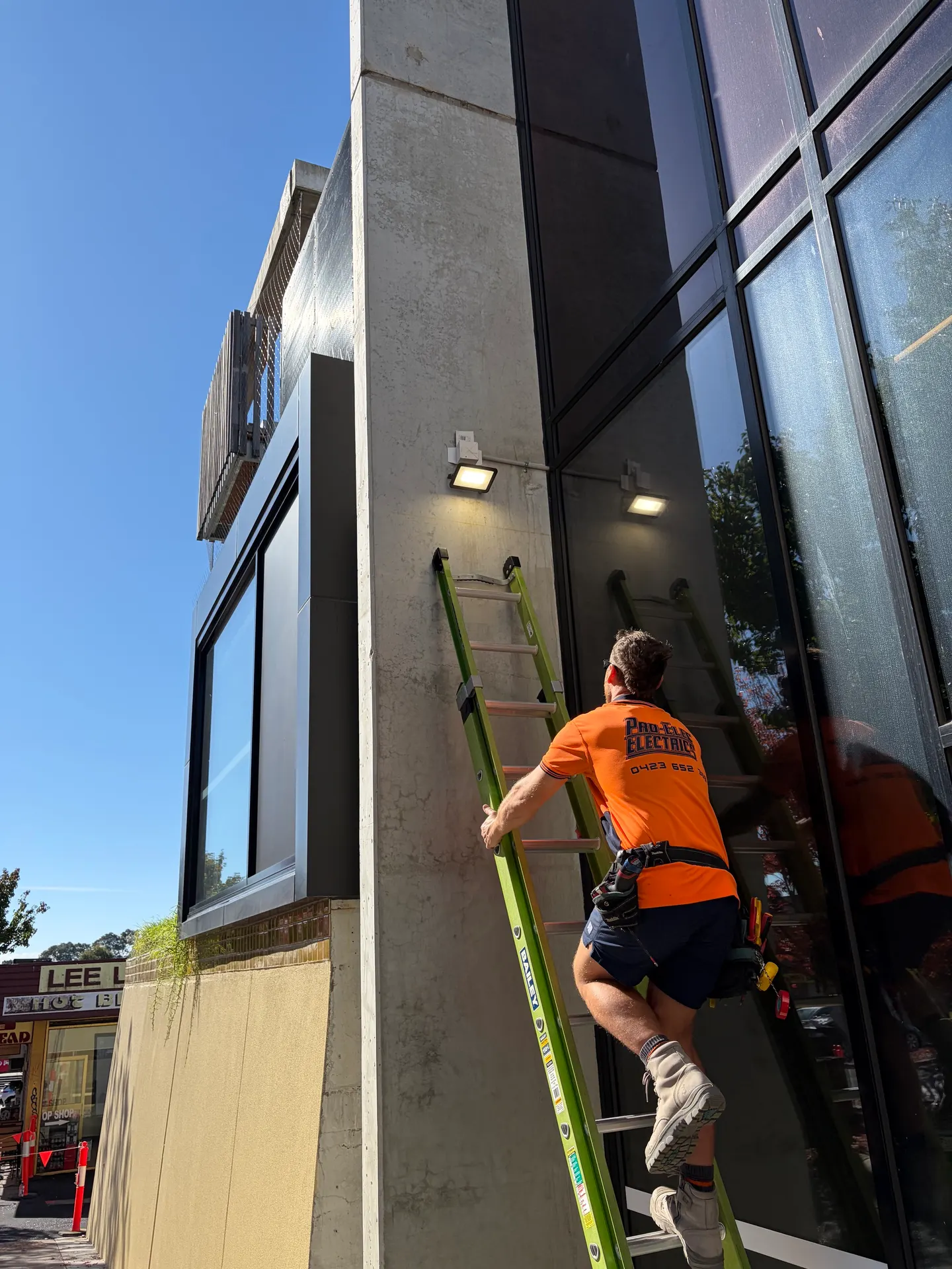 Pro-Elec electrician installing exterior wall lighting on a commercial shopfront